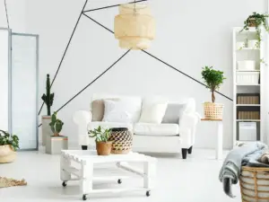 A modern living room in Ulcinj, Montenegro, with a white sofa, assorted pillows, and potted plants. A mobile coffee table sits in front, while black geometric lines highlight the wall—perfect for eco-conscious real estate properties like Ekosphere.