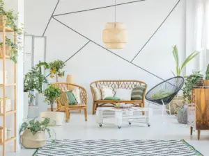 Bright living room with rattan furniture, green plants, and a geometric rug—a perfect showcase of real estate properties in Ulcinj, Montenegro. The white wall with black lines and Ekosphere touches create a fresh, modern vibe.