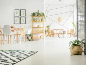 Bright, modern living and dining area in Ulcinj, Montenegro real estate properties, featuring light wood furniture, green plants, geometric wall art, a black and white patterned rug, and wicker chairs—all set against white walls and flooring.