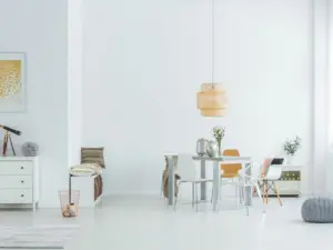 Bright, minimalist dining room in Ulcinj, Montenegro real estate properties, featuring a round white table, mixed chairs, pendant light, small bench with pillows, and gold decor accents like a dresser, telescope, and framed artwork.