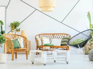 A bright living room in Ulcinj, Montenegro, with rattan furniture, green and white cushions, a black modern chair, a white wooden coffee table on wheels, potted plants, and a white wall with geometric black lines—perfect for ekosphere real estate properties.