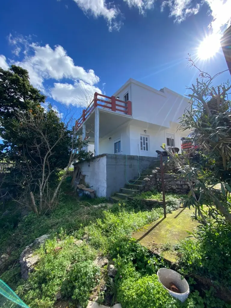 Stunning two-story white house with red balcony, sunlit yard on a grassy slope—prime Ulcinj real estate via montenegro-listings.me by ekosphere doo.