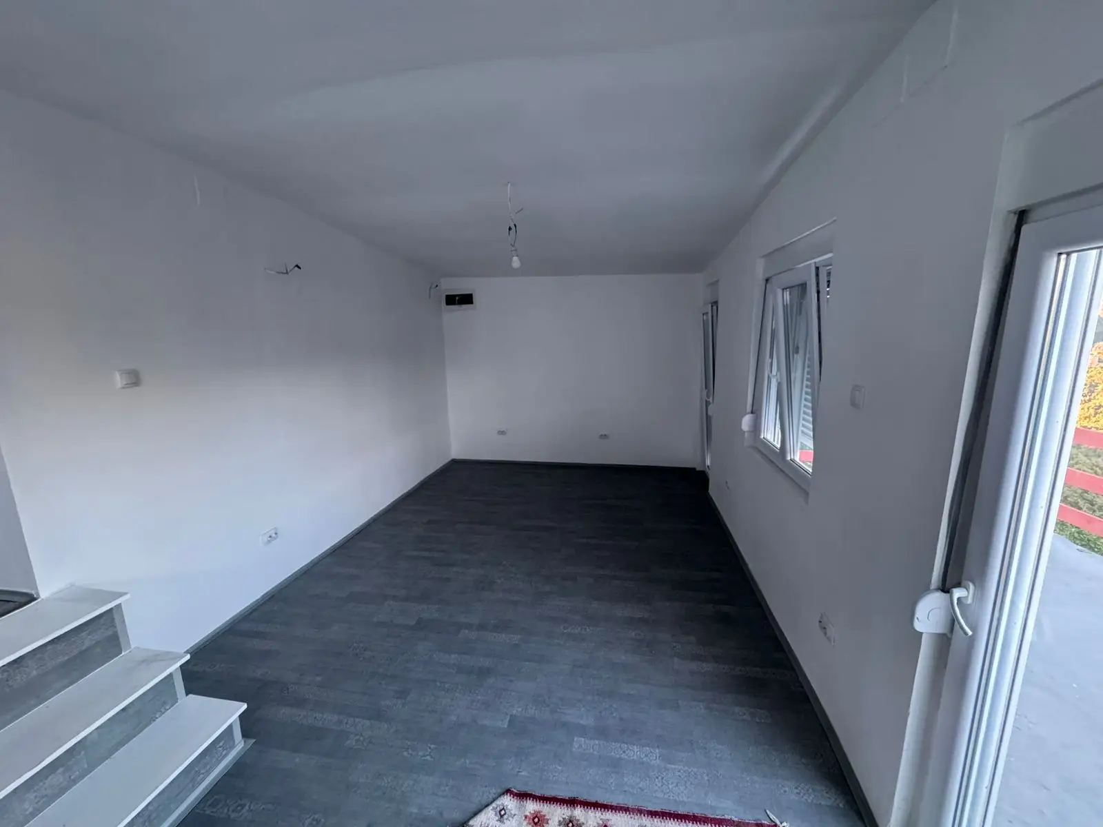 Modern investment opportunity in Ulcinj: bright room with white walls, dark floors, stairs, 3 windows, and glass door by ekosphere.