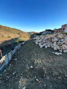 Prime Ulcinj land with development potential—clear lot, rock pile, fenced, scenic hills/homes. Montenegro-listings.me by ekosphere doo.