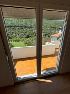 Modern Ulcinj property: glass doors open to tiled balcony, scenic green hills, red-roof views; ideal real estate at montenegro-listings.me.