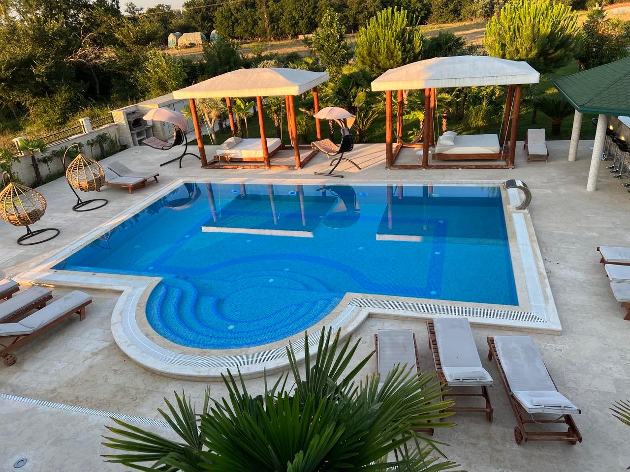 Luxurious pool oasis with blue tiles, lounge chairs, cabanas & chic seating&mdash;prime Ulcinj investment. Listed on montenegro-listings.me.