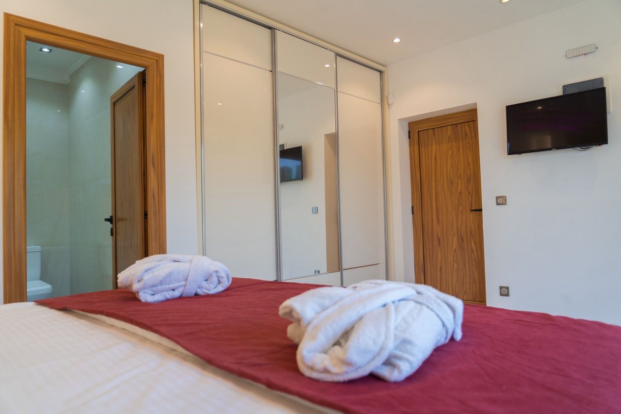 Modern Ulcinj property: elegant bedroom with red coverlet, bathrobes, premium finishes. Exclusive on montenegro-listings.me by Ekosphere DOO.