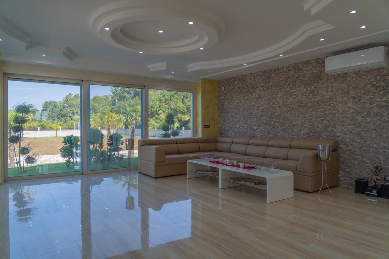 Modern Ulcinj living room with tan sectional, white coffee table, stone accent wall, and lush views&mdash;exclusive by montenegro-listings.me.