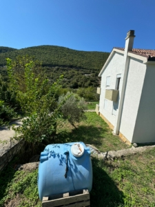 Charming white house with red roof, water tank, lush greenery, hills—prime Ulcinj real estate by ekosphere doo on montenegro-listings.me.
