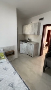 Modern kitchenette with light wood cabinets, tiled backsplash, and cozy sleeping area—ideal Ulcinj investment at montenegro-listings.me by ekosphere doo.