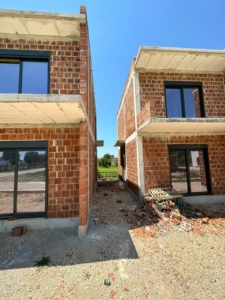 Prime Ulcinj investment: two unfinished brick homes with glass features, ideal for custom development. Listed by Ekosphere on montenegro-listings.me.