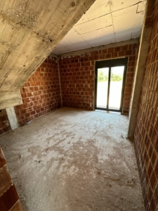 Spacious unfinished Ulcinj property with brick walls, concrete floor, and bright glass door—prime investment by ekosphere doo.