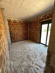 Spacious unfinished room in Ulcinj with red brick walls, concrete floor, large glass doors—prime investment at montenegro-listings.me by ekosphere doo.