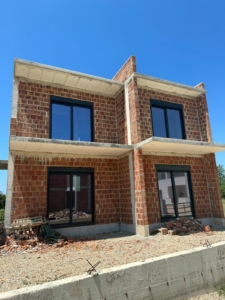 Modern two-story house under construction in Ulcinj, Montenegro—prime real estate with brick walls, large windows, and investment potential. Montenegro-listings.me by Ekosphere DOO.