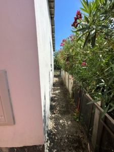 Charming walkway by a modern white building, lush gardens, and secure fencing—prime Ulcinj real estate via montenegro-listings.me by ekosphere doo.