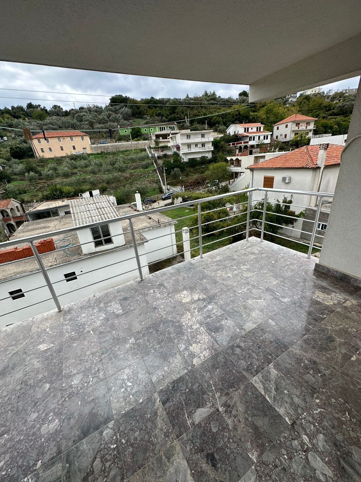 Spacious tiled balcony with metal railing, panoramic Ulcinj views of white and red-roofed homes, ideal for investment. Montenegro-listings.me by ekosphere doo.