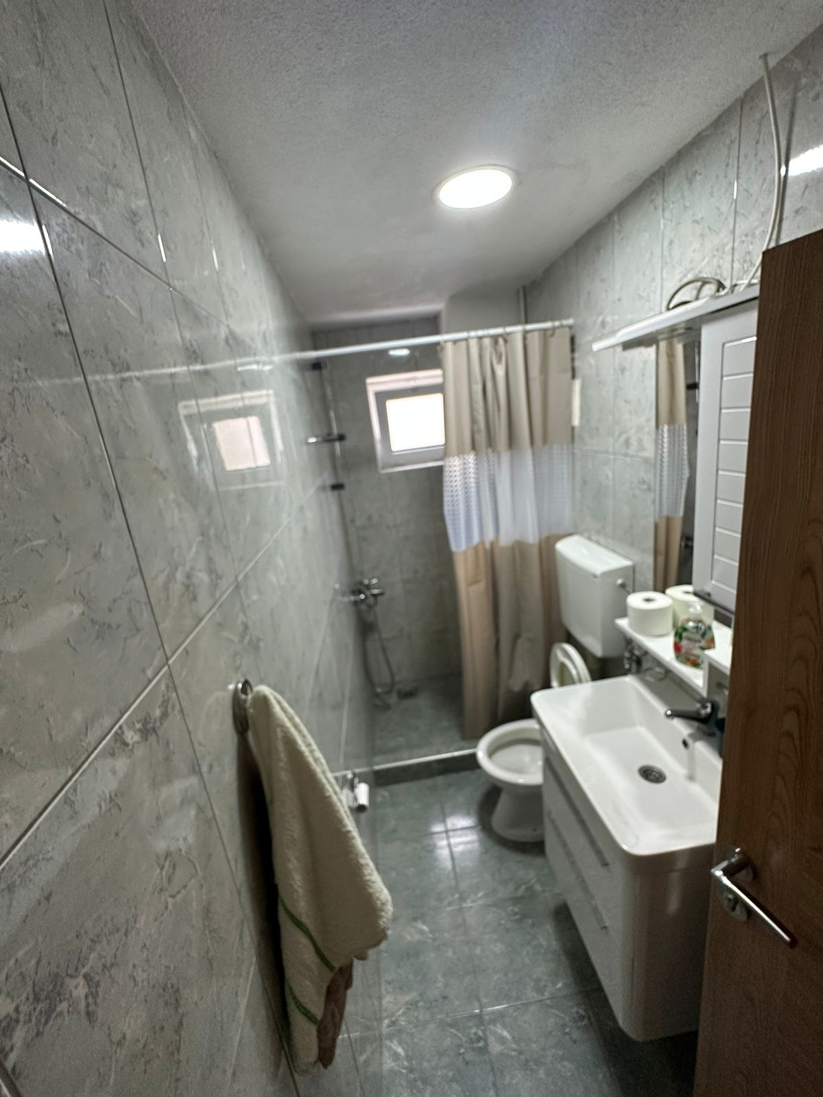 Modern gray-tiled bathroom with shower, toilet, sink, and mirror in Ulcinj property&mdash;exclusive on montenegro-listings.me by ekosphere doo.