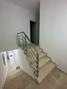Modern staircase with beige steps, metal handrail, and bright white walls—ideal Ulcinj real estate by ekosphere doo. Invest today!.