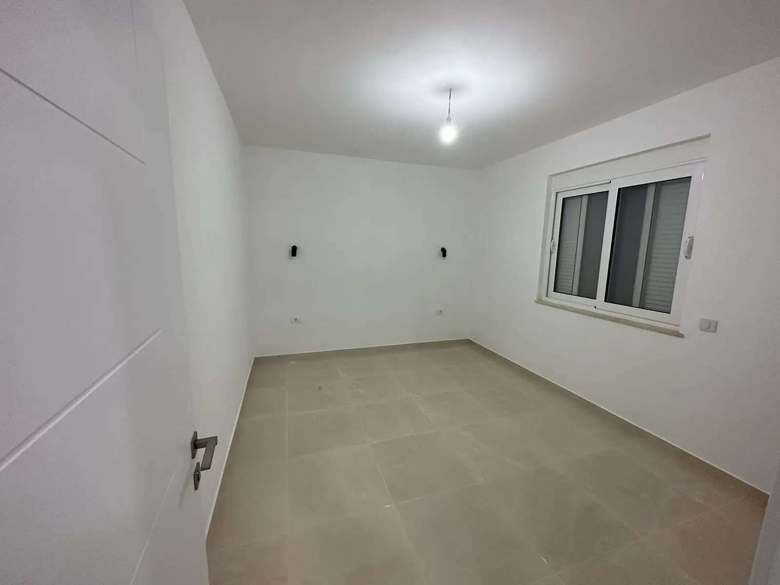 Modern, sunlit room in Ulcinj, Montenegro—ideal investment. White walls, tiled floor, window. Exclusive on montenegro-listings.me by Ekosphere doo.