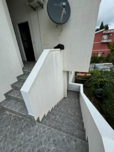 Premium Ulcinj property: tiled stairs, white wall with satellite, red building and lush greenery. montenegro-listings.me by ekosphere doo.