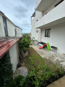 Charming Ulcinj home for sale: grassy backyard, potted plants, patio with sofa, grill, kids’ slide. Montenegro-listings.me by Ekosphere.