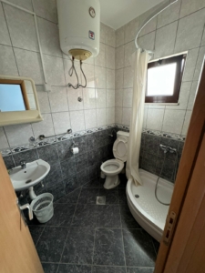 Modern small bathroom in Ulcinj, Montenegro property—gray tiles, compact shower, wall sink; on montenegro-listings.me by Ekosphere doo.