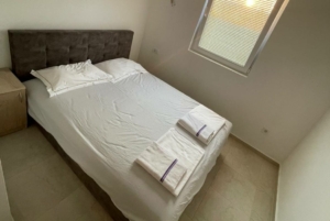 Modern Ulcinj bedroom with double bed, crisp linens, nightstand, window—prime real estate by ekosphere doo on montenegro-listings.me.