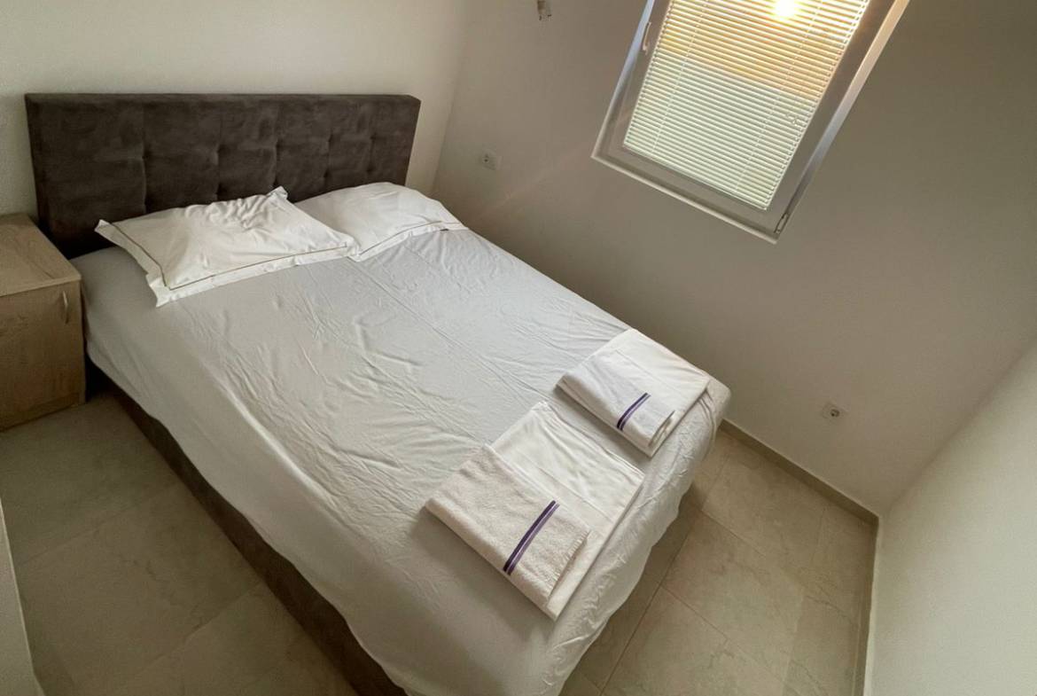 Modern Ulcinj bedroom with double bed, crisp linens, nightstand, window&mdash;prime real estate by ekosphere doo on montenegro-listings.me.