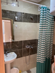 Modern Ulcinj bathroom with stylish beige/dark brown tiles, shower, sink, and water heater—ideal real estate on montenegro-listings.me.