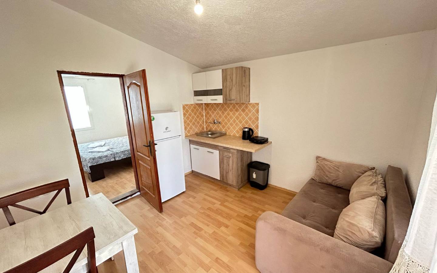 Modern Ulcinj apartment for sale: open kitchen, brown sofa, dining area, wood floors. Invest via montenegro-listings.me by ekosphere doo.