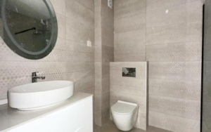 Stylish modern bathroom in luxury Ulcinj property: beige tiles, wall-mounted toilet, round mirror, and chic vanity. montenegro-listings.me by ekosphere doo.