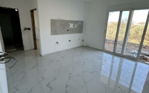 Modern Ulcinj property: bright white walls, marble tiles, glass doors, kitchen-ready space—exclusive at montenegro-listings.me by Ekosphere doo.