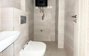 Modern tiled bathroom with wall-mounted toilet, corner sink, and water heater—ideal Ulcinj Montenegro investment. Montenegro-listings.me by Ekosphere.