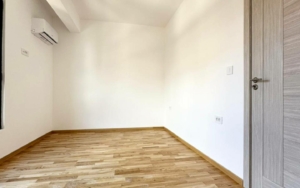 Modern, sunlit room with wooden flooring, white walls, AC, ideal Ulcinj investment. Listed on montenegro-listings.me by Ekosphere.