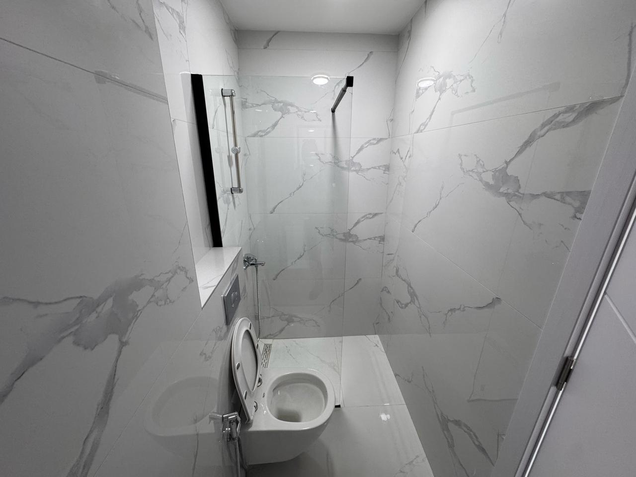 Modern bathroom in Ulcinj with marble tiles, wall-mounted toilet, glass partition&mdash;ideal investment at montenegro-listings.me by ekosphere doo.