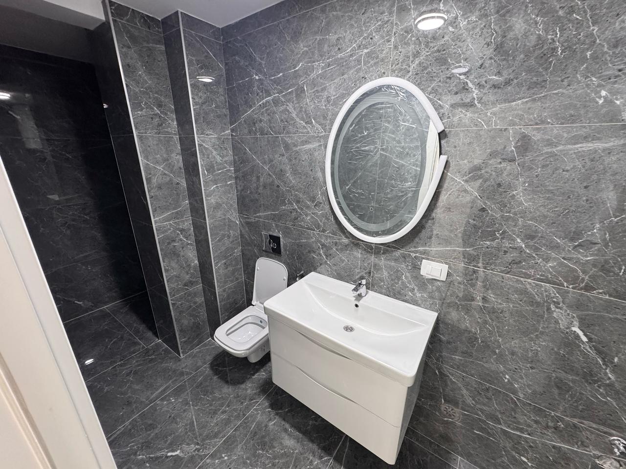 Luxurious modern bathroom with dark marble, wall-mounted toilet, elegant vanity and mirror in Ulcinj&mdash;featured on montenegro-listings.me.