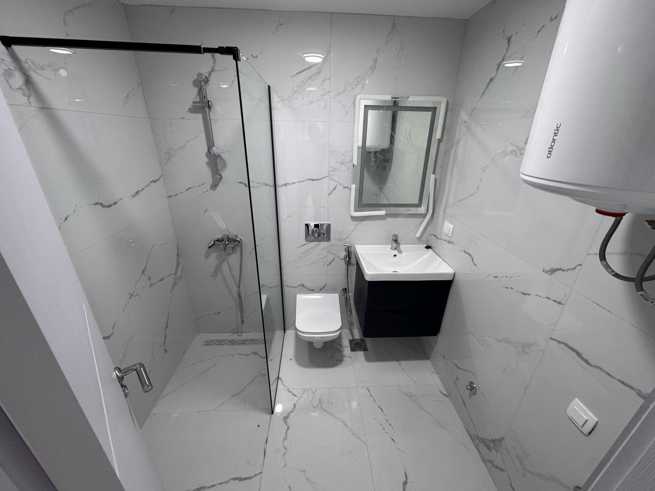 Sleek Ulcinj bathroom with gray marble, wall-mounted toilet, floating sink, glass shower&mdash;exclusive at montenegro-listings.me by Ekosphere.