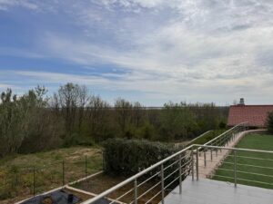 Spacious tiled balcony with metal railing, lush lawn, and red-roofed house in Ulcinj, Montenegro—exclusive on montenegro-listings.me by ekosphere doo.