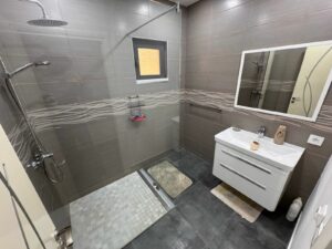 Stylish Ulcinj bathroom: gray tiles, walk-in shower, rainfall heads, vanity, mirror—premium real estate by montenegro-listings.me.
