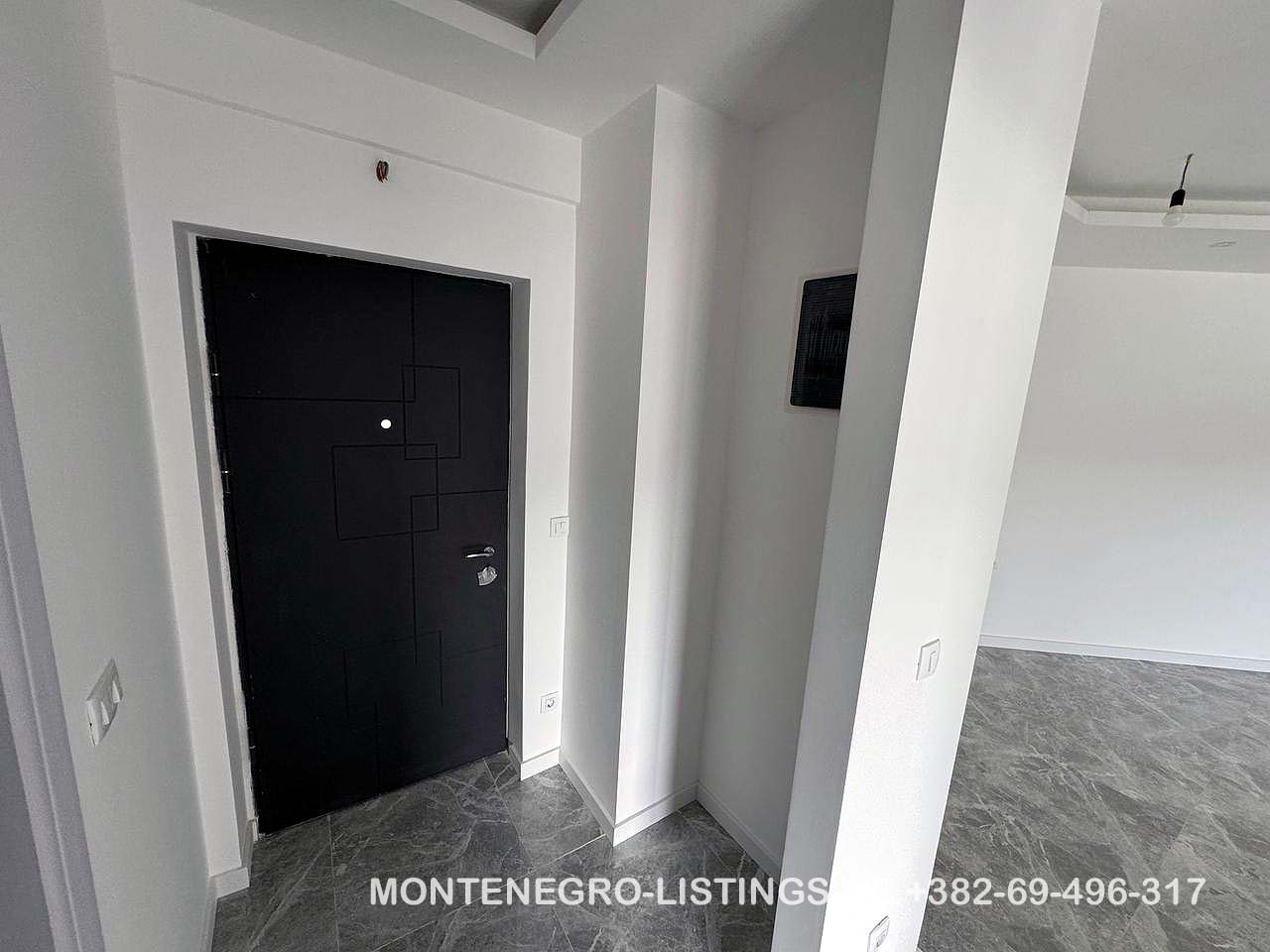 Contemporary Ulcinj apartment entry: sleek black door, white walls, grey tiled floor. Invest with montenegro-listings.me by ekosphere doo.