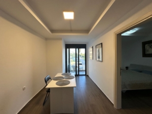 Modern minimalist dining area with sleek white table, balcony access, quality wood floors—ideal Ulcinj real estate at montenegro-listings.me (a project of ekosphere doo).