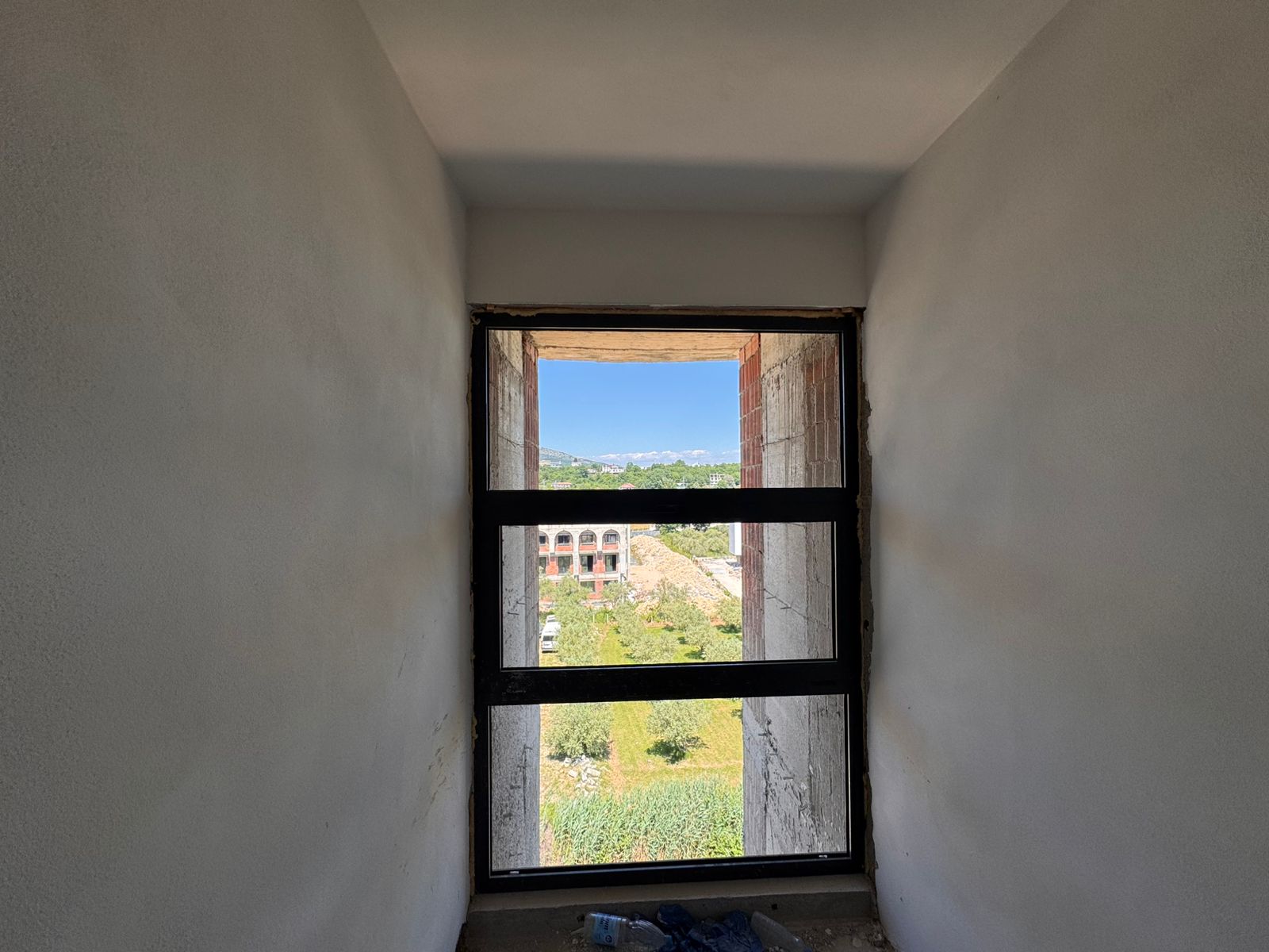 Bright window view reveals lush greenery, Ulcinj properties, mountain vistas&mdash;invest in Montenegro real estate via montenegro-listings.me.