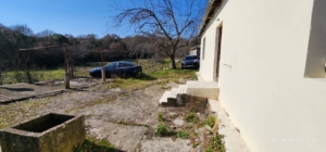 Bright concrete yard next to a pale building with steps, cars, and hills—prime Ulcinj real estate on montenegro-listings.me by ekosphere doo.
