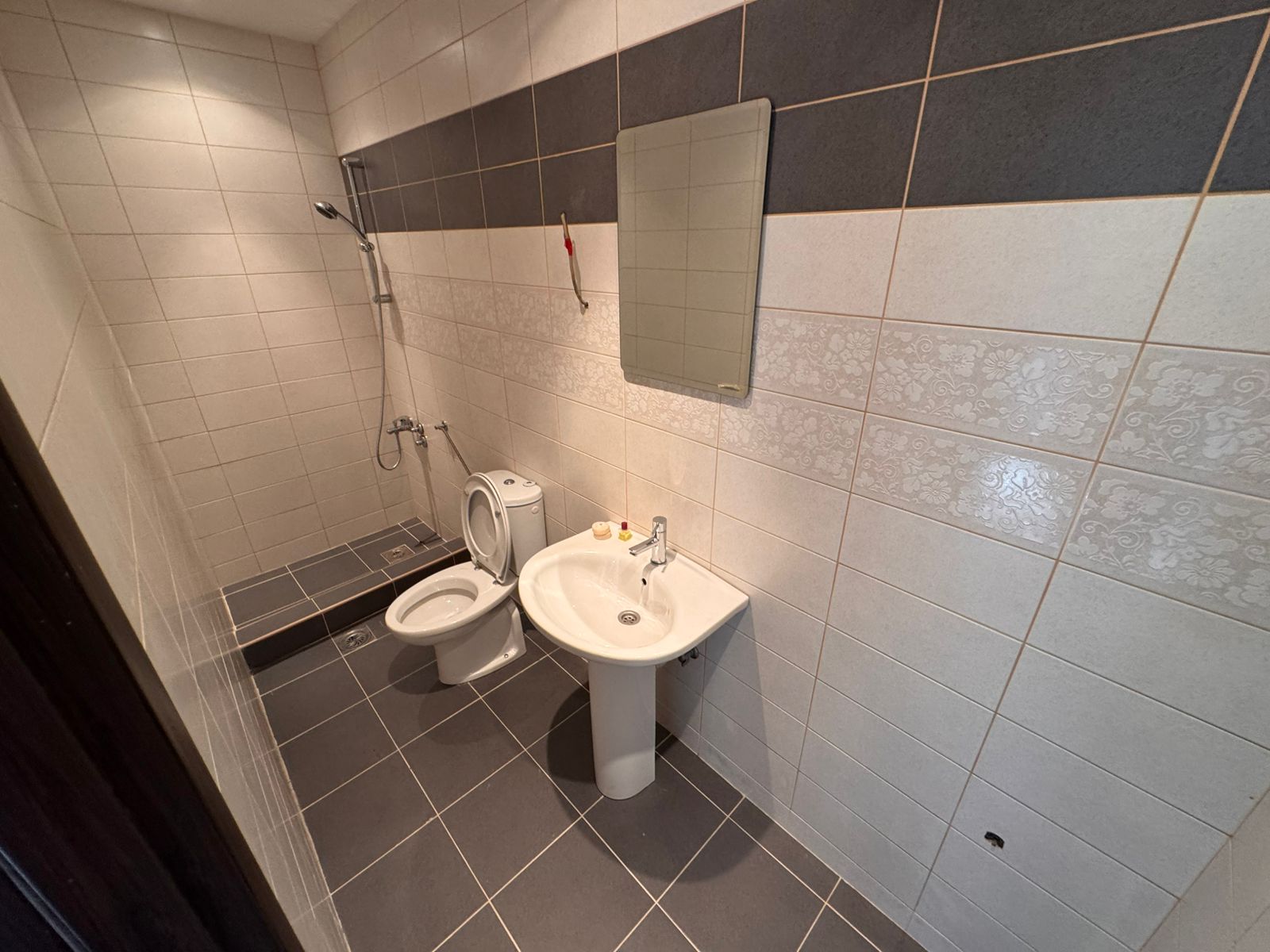 Modern Ulcinj Montenegro property bathroom: tiled in gray and white, with shower, sink, and mirror. Discover more on montenegro-listings.me by ekosphere doo.