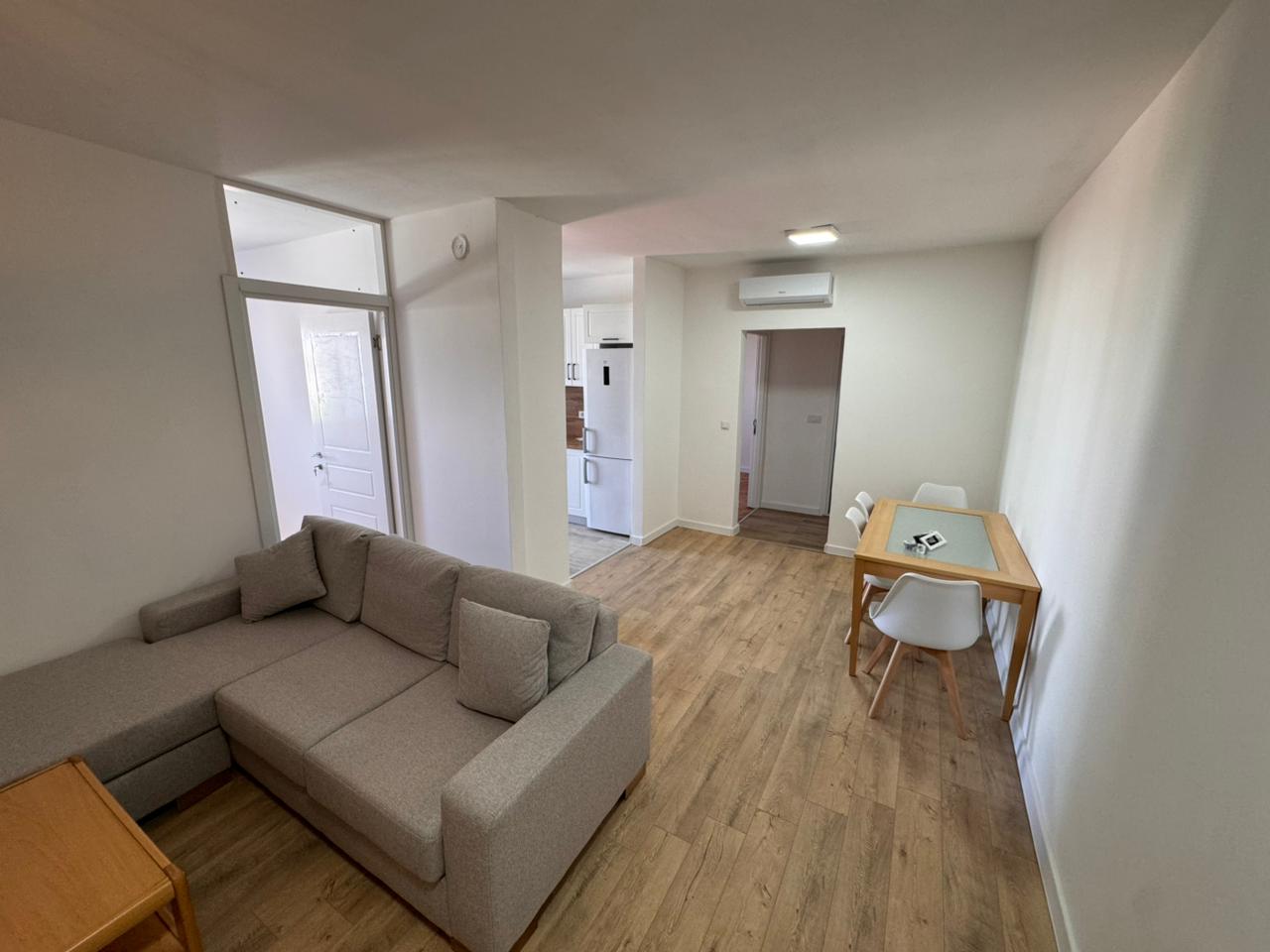 Modern Ulcinj apartment: bright open-plan living with light wood floors, L-sofa, dining area—listed by montenegro-listings.me (EkoSphere).