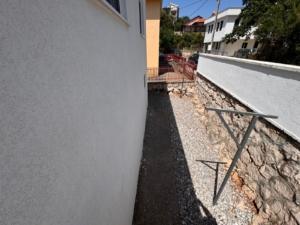 Prime Ulcinj property: gravel walkway & concrete path between buildings, metal structure, stone wall—exclusive at montenegro-listings.me by ekosphere doo.
