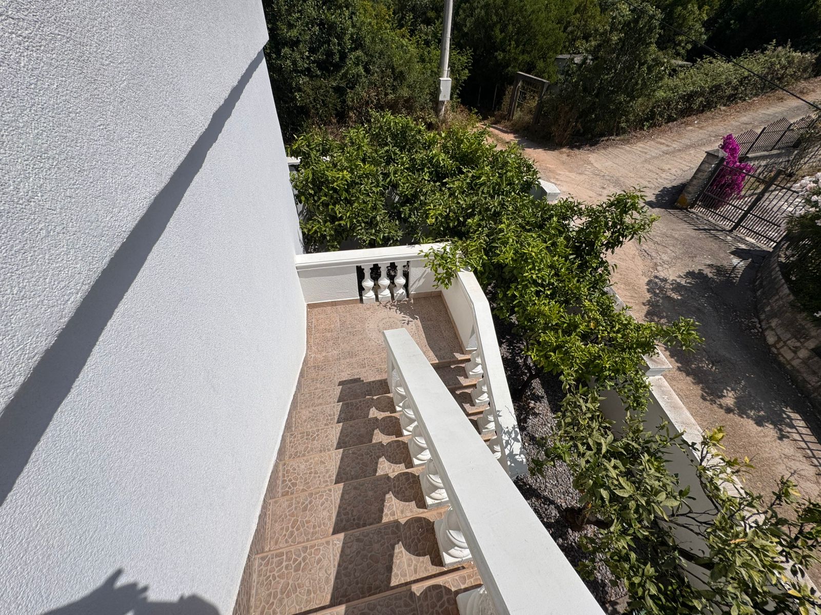 Modern outdoor staircase with white railings, brown tiles, and lush greenery&mdash;prime Ulcinj property via montenegro-listings.me by Ekosphere.