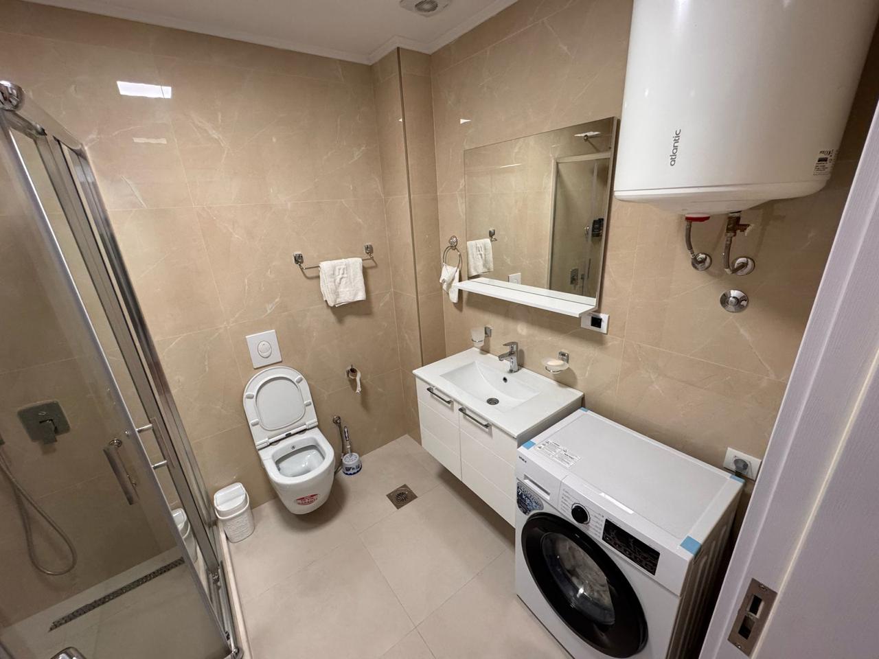 Modern Ulcinj bathroom with beige tiles, shower, vanity, washer&mdash;premium real estate at montenegro-listings.me by Ekosphere doo.