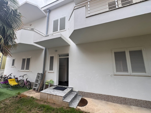 Modern white two-story home in Ulcinj, with porch, open entry, child-friendly lawn by palm tree. Listed on montenegro-listings.me by ekosphere doo.