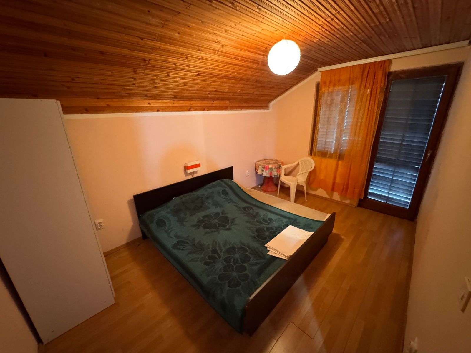 Inviting Ulcinj bedroom with sloped wood ceiling, double bed, orange curtains&mdash;ideal Montenegro investment. Listed on montenegro-listings.me by Ekosphere doo.